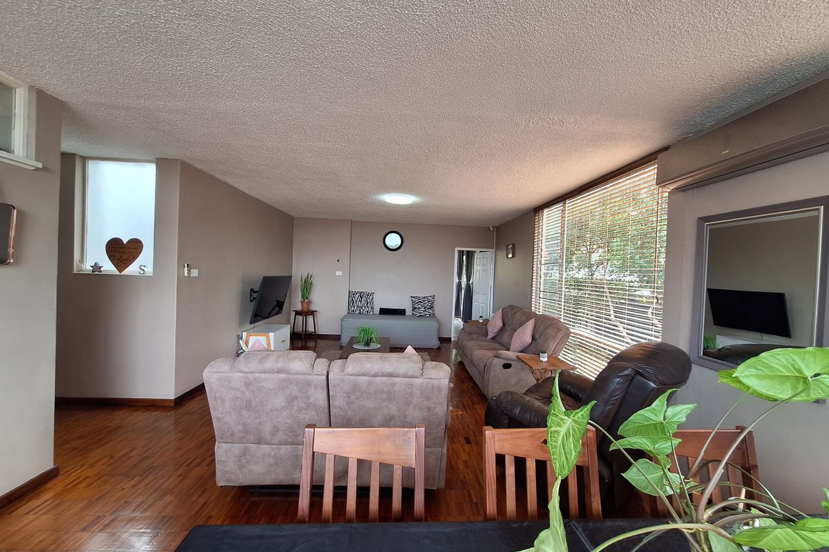 Spacious living room featuring hardwood flooring, large windows with venetian blinds, and an integrated air conditioning unit.