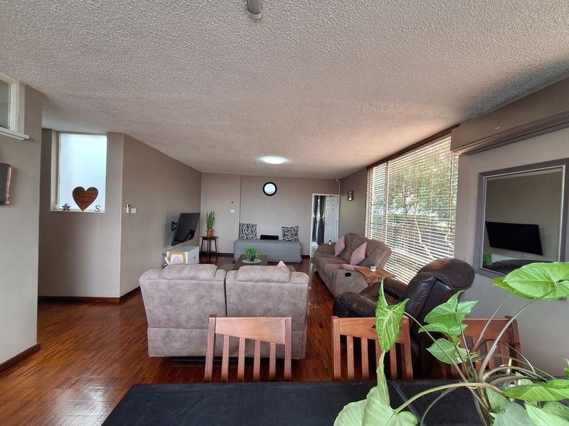 Spacious living room featuring hardwood flooring, large windows with venetian blinds, and an integrated air conditioning unit.