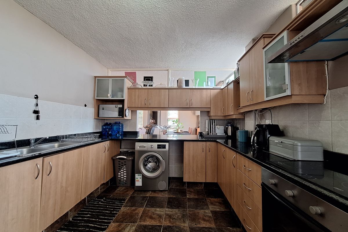 Functional kitchen featuring wood-finish cabinetry, granite countertops, integrated oven and hob, and tiled flooring with a dedicated space for a washing machine.