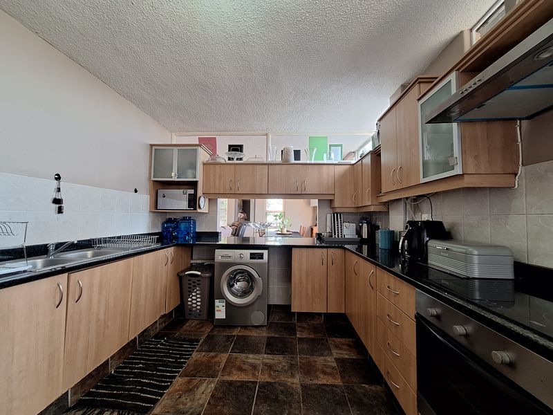 Functional kitchen featuring wood-finish cabinetry, granite countertops, integrated oven and hob, and tiled flooring with a dedicated space for a washing machine.