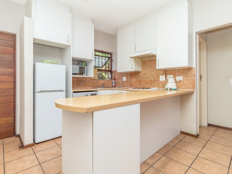 Functional kitchen featuring white built-in cabinetry, a breakfast bar, tiled backsplash, and ceramic floor tiles.