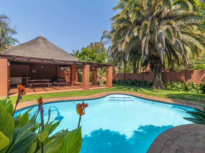 A well-maintained outdoor area featuring a swimming pool, landscaped garden, and a spacious thatched lapa with a built-in counter for outdoor entertaining.