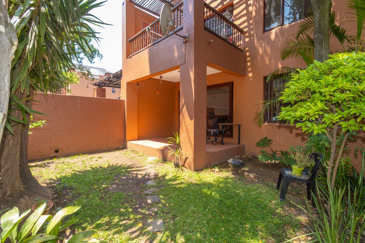 Rear view of the apartment featuring a ground-floor covered patio, an upper-level balcony with wooden balustrades, and a private garden area.