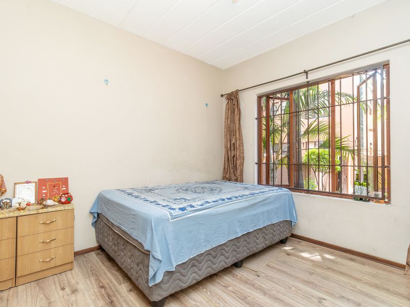 A bedroom featuring laminate flooring and a window with security bars. The space requires cosmetic updates to the walls and ceiling.