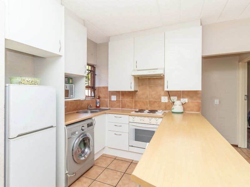 Compact kitchen featuring white cabinetry, laminate countertops, tiled backsplash, and integrated appliances including an oven, hob, and extractor fan.
