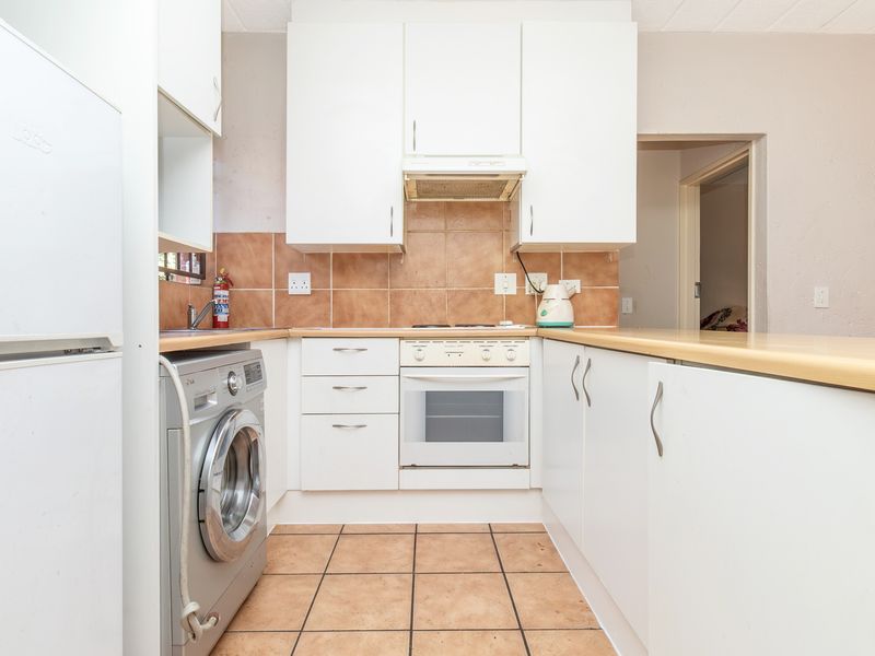 A functional kitchen featuring white cabinetry, tiled backsplash, built-in oven with extractor fan, and tiled flooring, offering a practical layout for daily use.