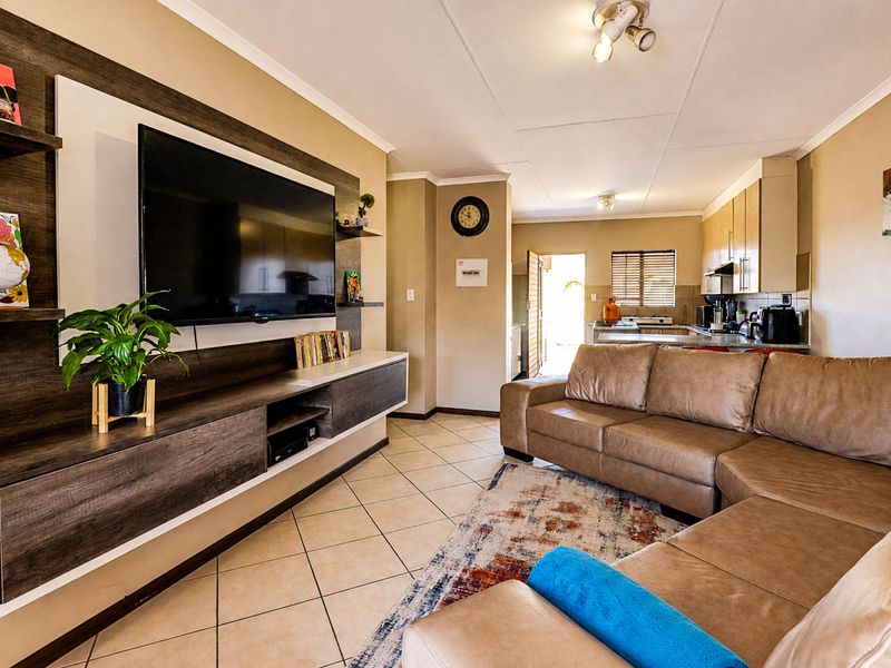 An open-plan living area featuring ceramic floor tiles, a built-in media console, and a functional kitchen with cabinetry and countertops.