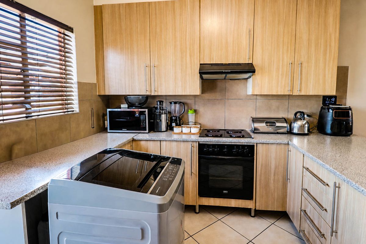Functional kitchen featuring light wood-grain cabinetry, granite countertops, built-in oven with hob, extractor fan, and tiled backsplash.