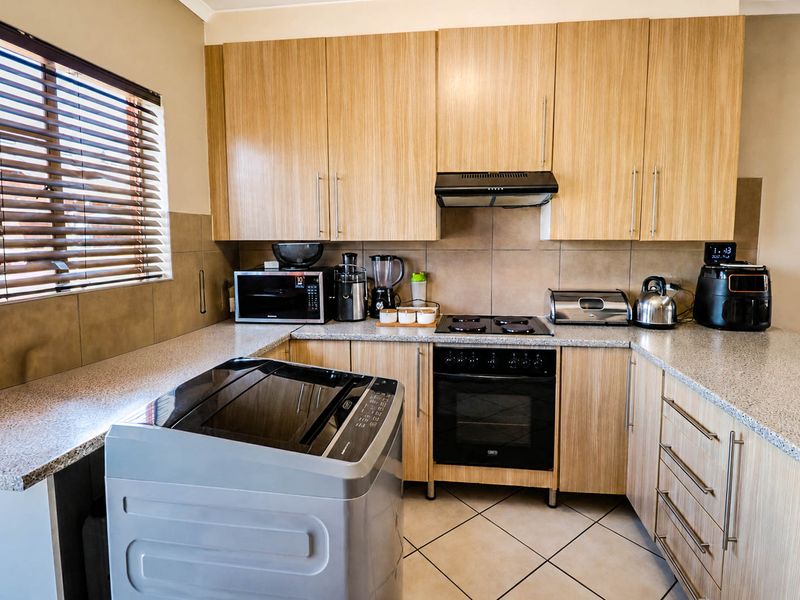 Functional kitchen featuring light wood-grain cabinetry, granite countertops, built-in oven with hob, extractor fan, and tiled backsplash.