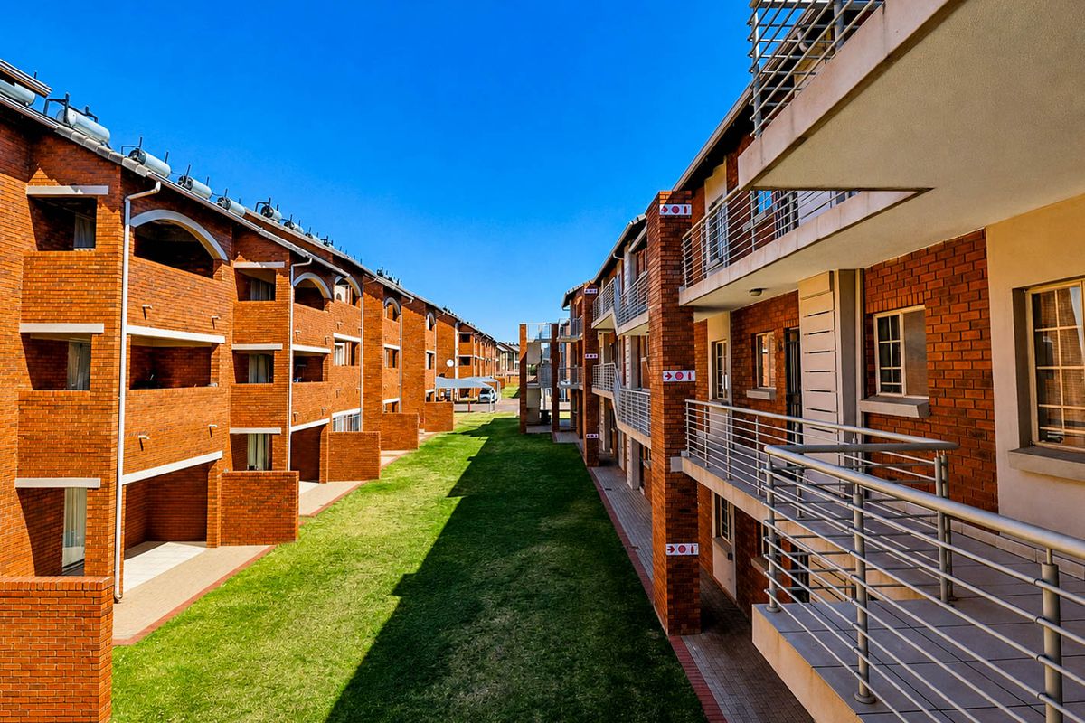 Exterior view of a townhouse complex featuring face brick facades, private balconies with metal railings, solar water heaters, and a well-maintained communal lawn area.