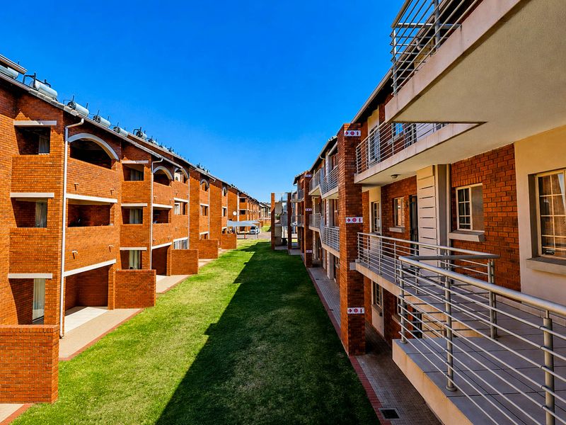 Exterior view of a townhouse complex featuring face brick facades, private balconies with metal railings, solar water heaters, and a well-maintained communal lawn area.