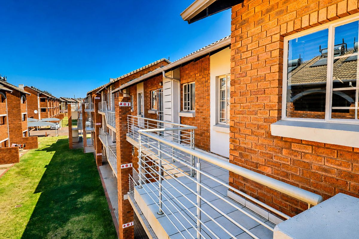 A view of the townhouse complex exterior featuring face brick facades, tiled balconies with metal railings, and communal garden space.