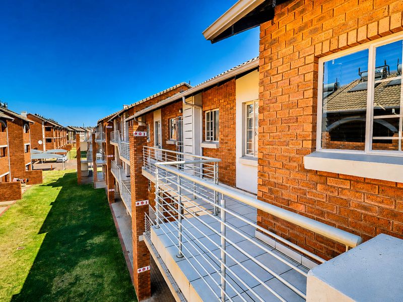 A view of the townhouse complex exterior featuring face brick facades, tiled balconies with metal railings, and communal garden space.