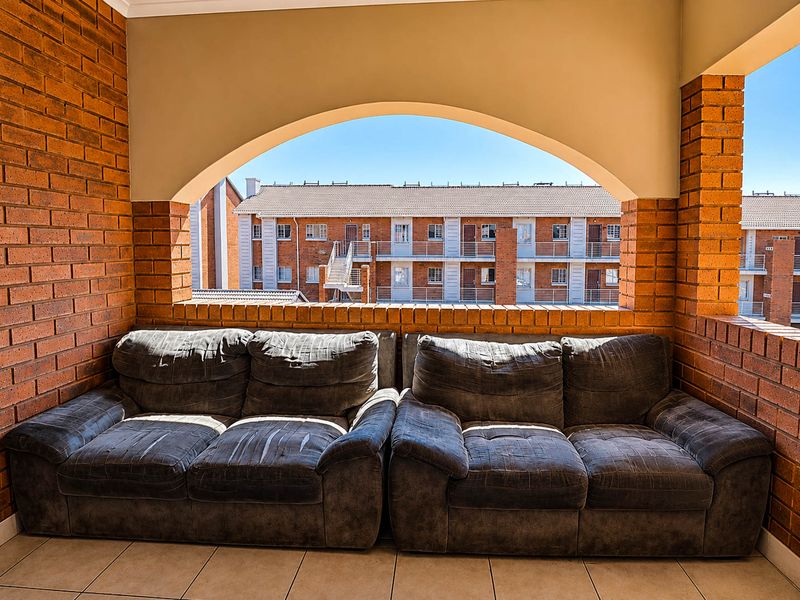 A covered balcony featuring exposed brick walls, an arched architectural opening, and tiled flooring, offering a view of the surrounding townhouse complex.