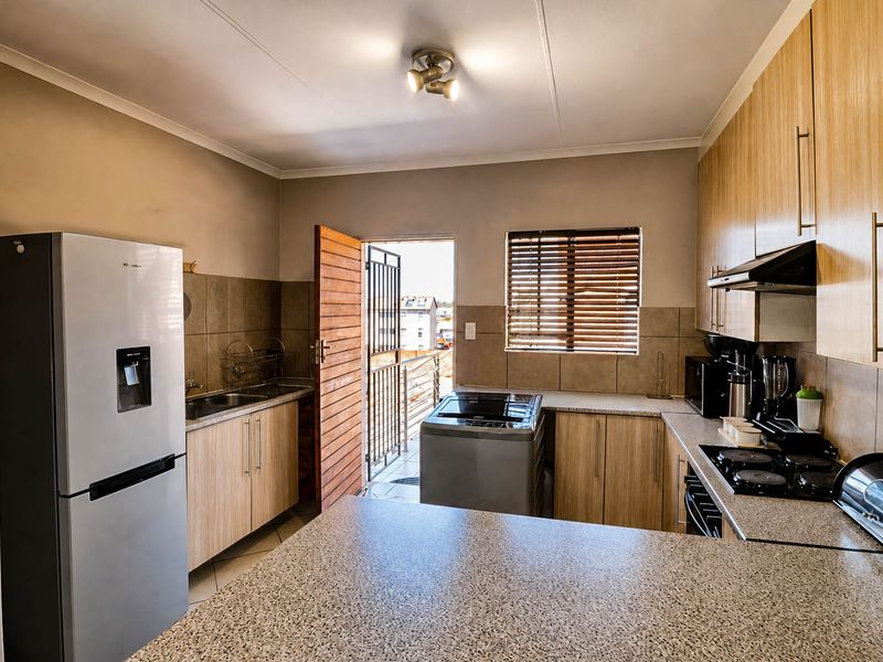 Functional kitchen featuring laminate cabinetry, stone-look countertops, built-in hob with extractor, and direct access to an outdoor area.