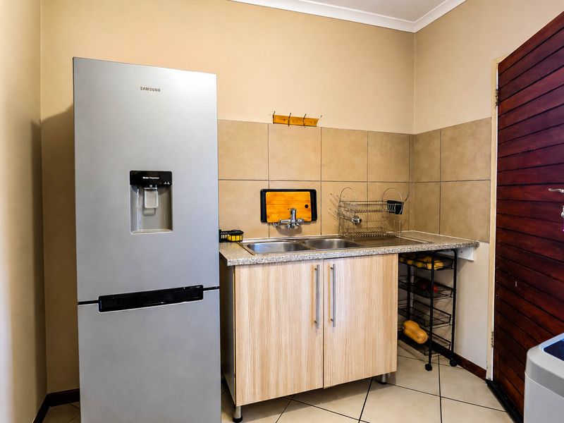 A functional laundry area featuring a double basin sink, tiled splashback, laminate cabinetry, and durable tiled flooring.
