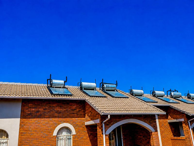 Exterior view of a townhouse featuring a face brick facade, tiled roof, and multiple solar water heating units installed.
