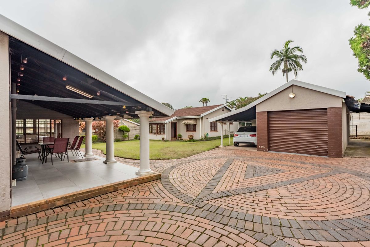 Spacious rear exterior featuring a covered patio with tiled flooring, a paved driveway, a garage, and a carport set within a landscaped garden area.