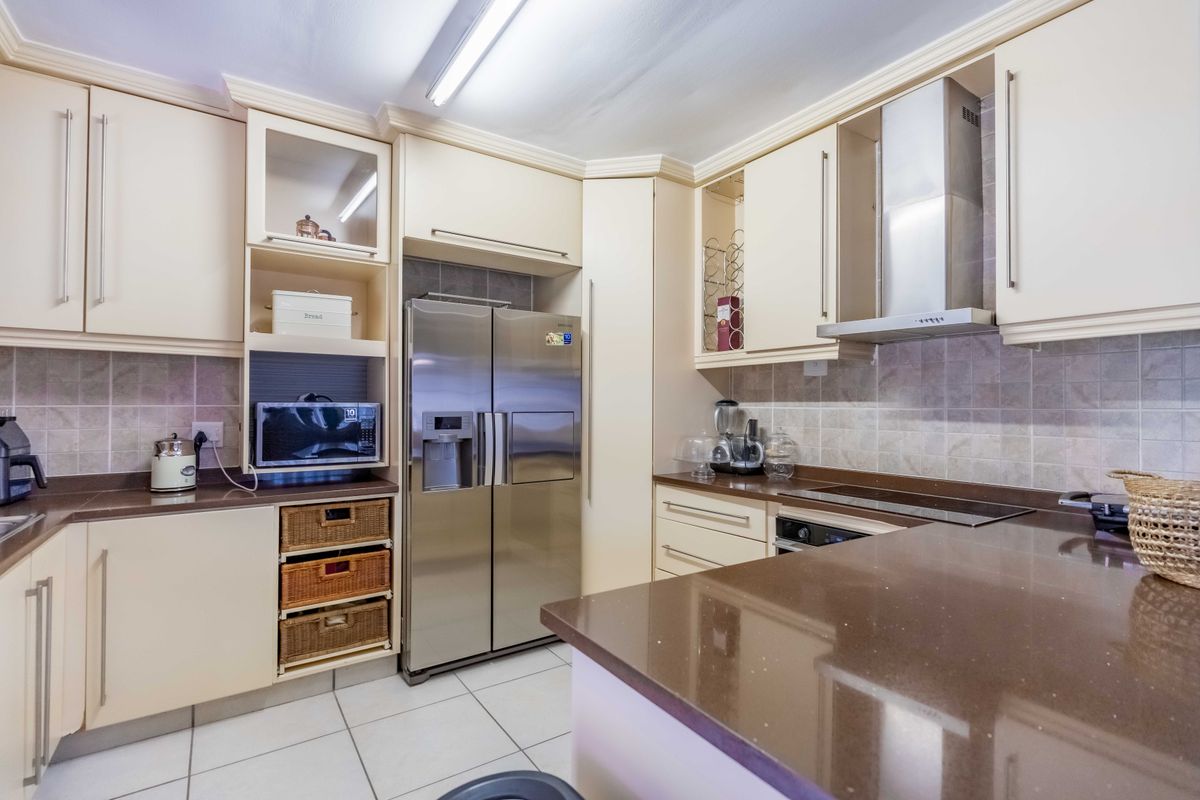 A functional kitchen featuring cream cabinetry, brown stone countertops, tiled backsplash, and integrated stainless steel appliances.