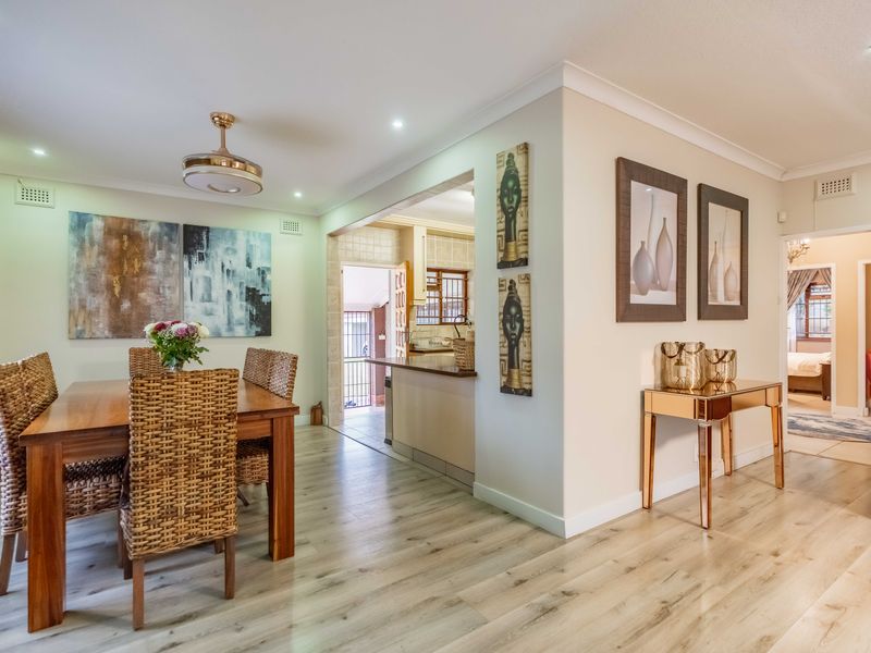 An open-plan dining area featuring light wood-look laminate flooring, recessed lighting, and a seamless transition into the adjacent kitchen space.