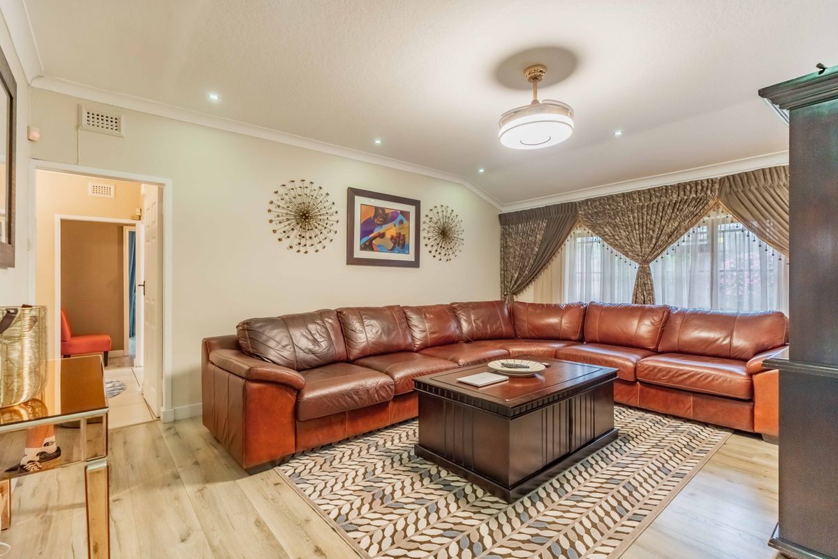A well-maintained living room featuring light-toned laminate flooring, recessed downlighting, and coved cornicing, creating a comfortable and inviting space.