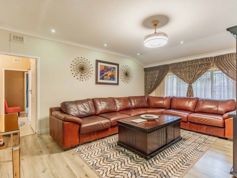 A well-maintained living room featuring light-toned laminate flooring, recessed downlighting, and coved cornicing, creating a comfortable and inviting space.