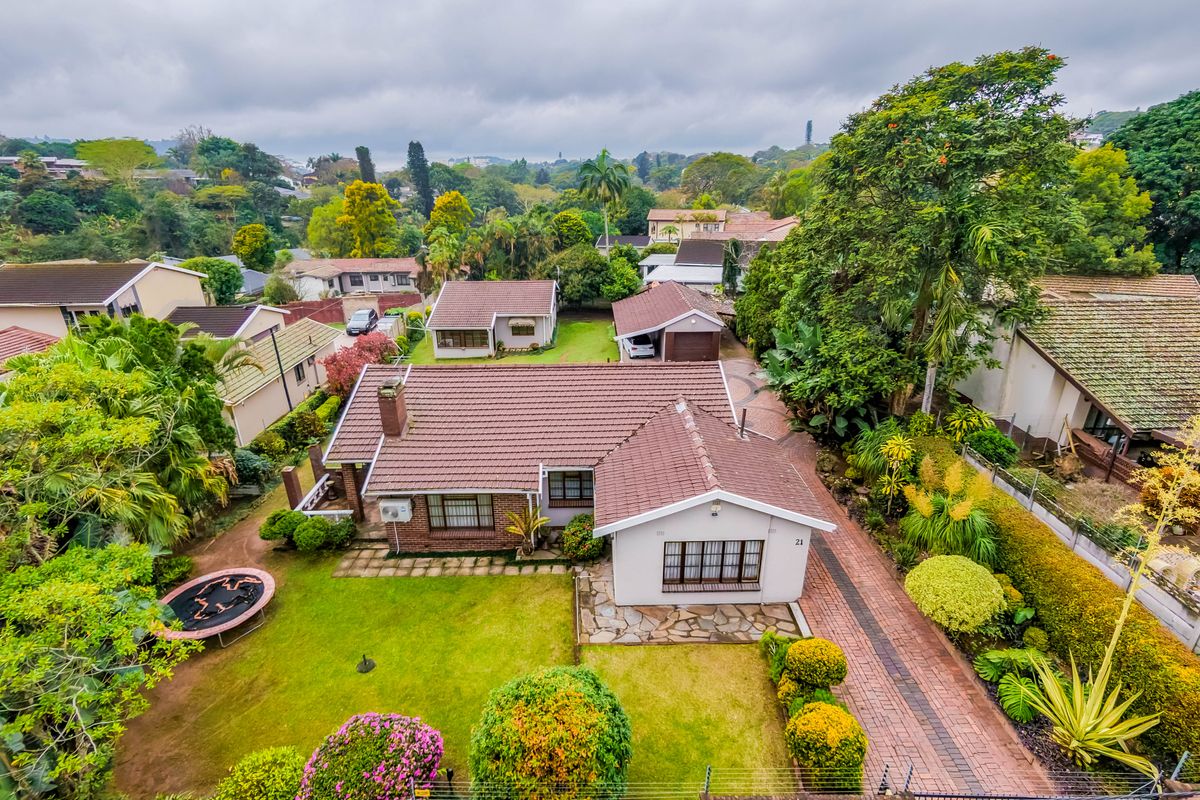 Aerial view of a residential property featuring a tiled roof, paved driveway, stone patio, and established garden in a suburban setting.
