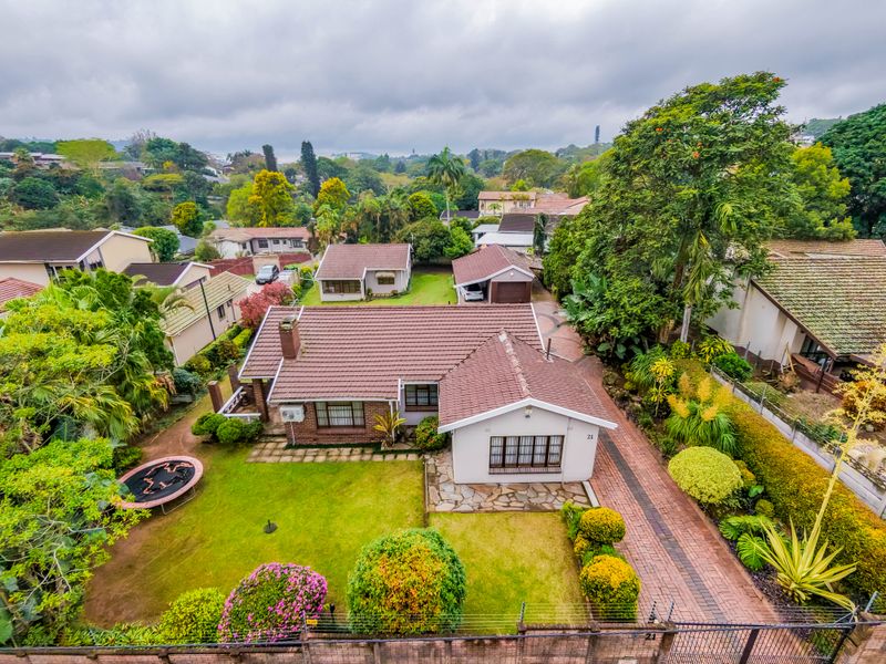 Aerial view of a residential property featuring a tiled roof, paved driveway, stone patio, and established garden in a suburban setting.