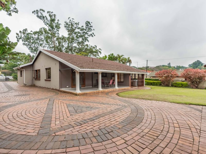 A well-maintained single-story house featuring a spacious brick-paved driveway, a covered patio with classic columns, and a neat surrounding garden.