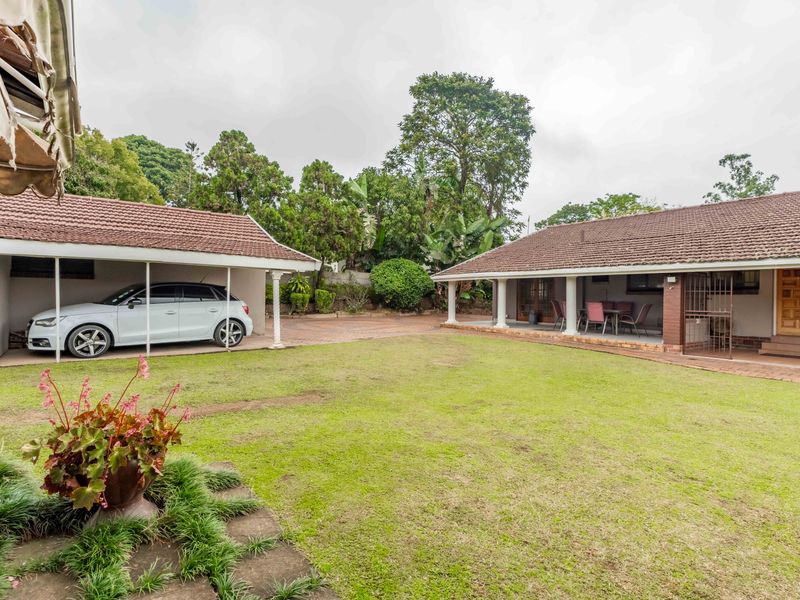 Spacious rear garden featuring a lawn, brick-paved areas, a covered carport, and a covered patio space.