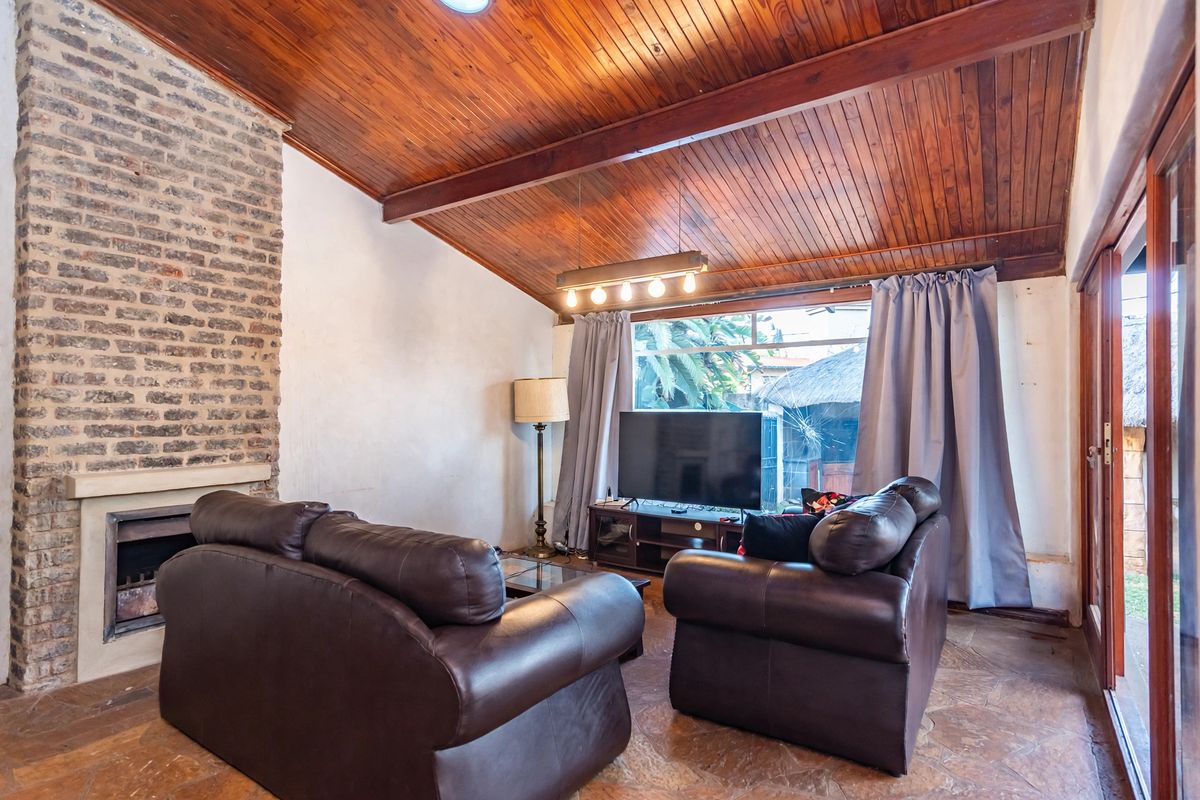 Living room featuring a vaulted timber ceiling, exposed brick fireplace, and flagstone flooring with direct access to the outdoor area through sliding glass doors.