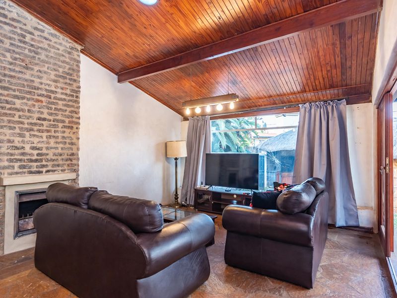 Living room featuring a vaulted timber ceiling, exposed brick fireplace, and flagstone flooring with direct access to the outdoor area through sliding glass doors.