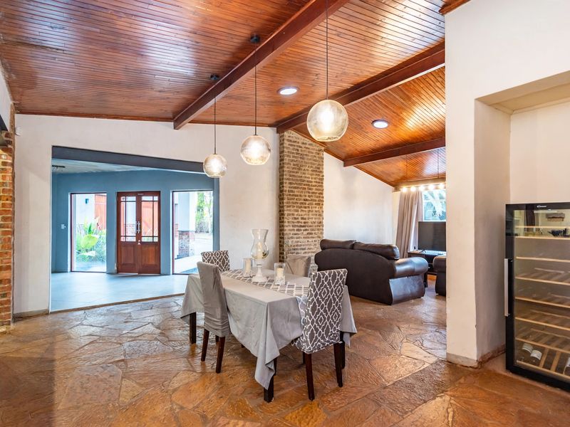 Spacious open-plan living and dining area featuring a vaulted timber ceiling, rustic stone flooring, and a prominent brick fireplace.