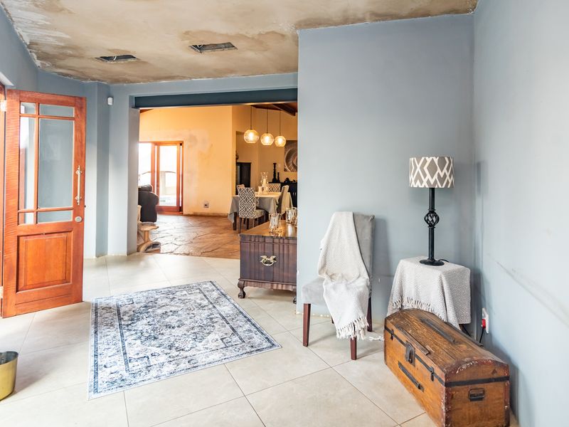 Entrance hall featuring tiled flooring and a timber door, leading into an open-plan living area. The ceiling requires repair and cosmetic attention.