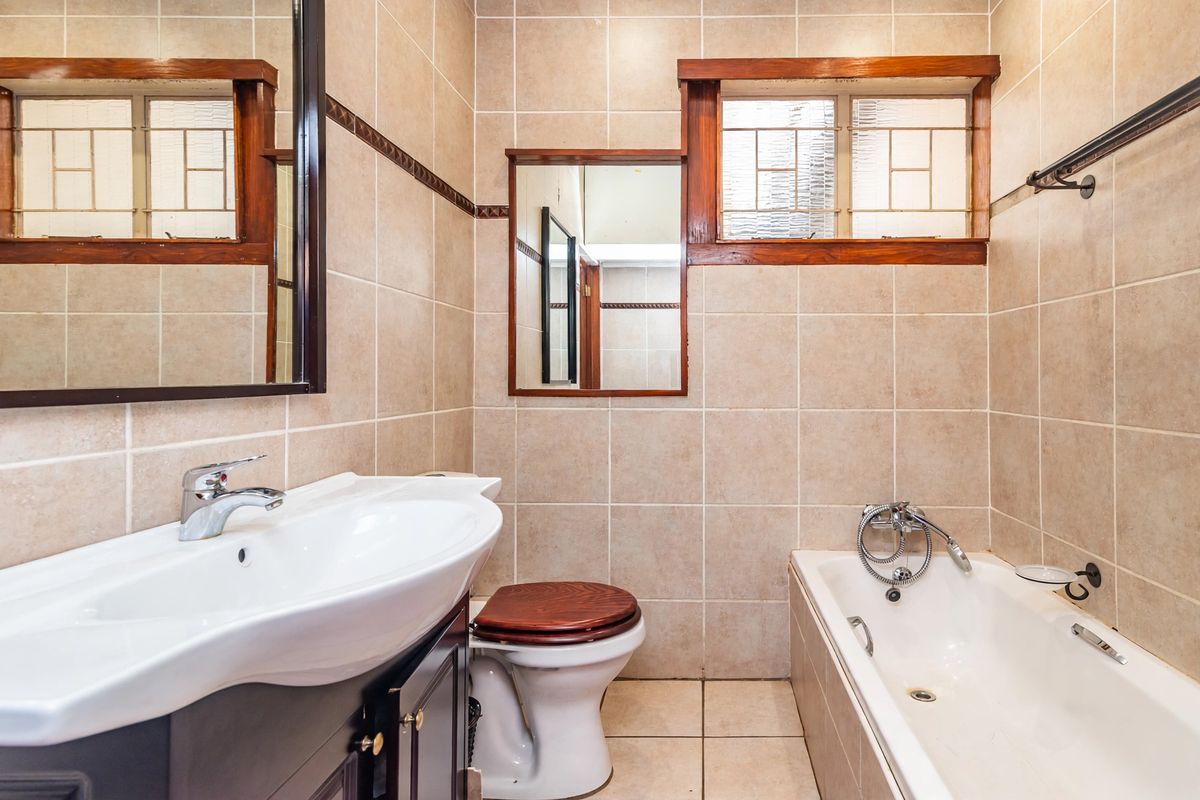 A functional bathroom featuring a vanity cabinet, bathtub with handheld shower, and neutral wall tiling with timber-framed windows.