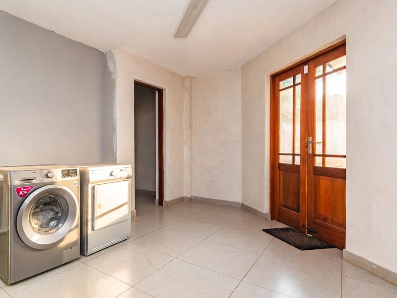 A functional laundry area featuring tiled flooring and timber-framed glass double doors, currently awaiting final wall finishing and paint.