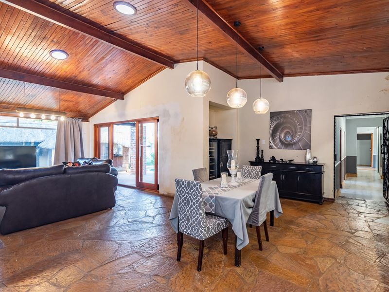 Spacious open-plan living and dining area featuring a vaulted timber ceiling, flagstone flooring, and direct access to the outdoor patio through sliding glass doors.