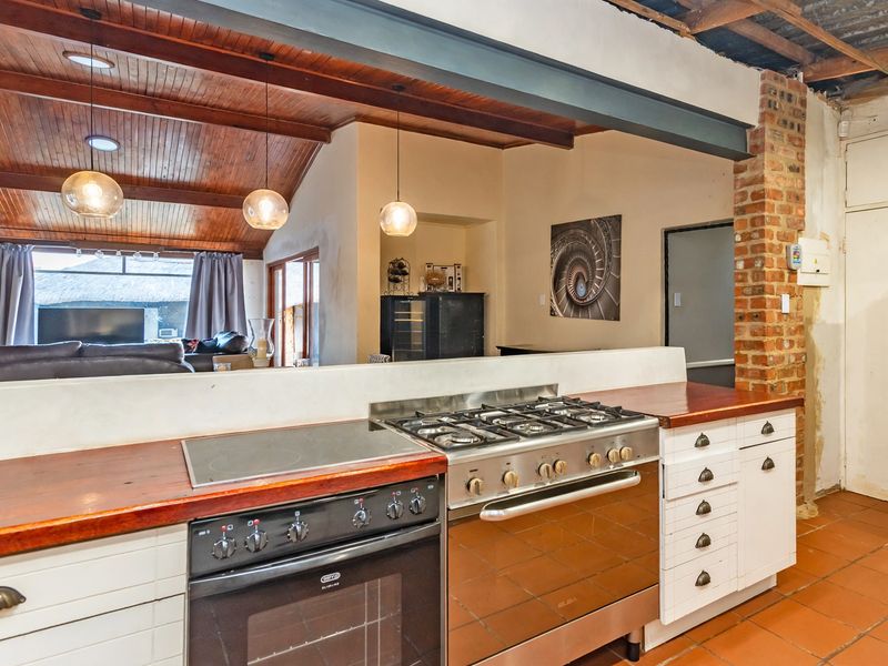 Open-plan kitchen featuring timber countertops, dual cooking appliances, and exposed brickwork, flowing into a living area with a vaulted timber ceiling.