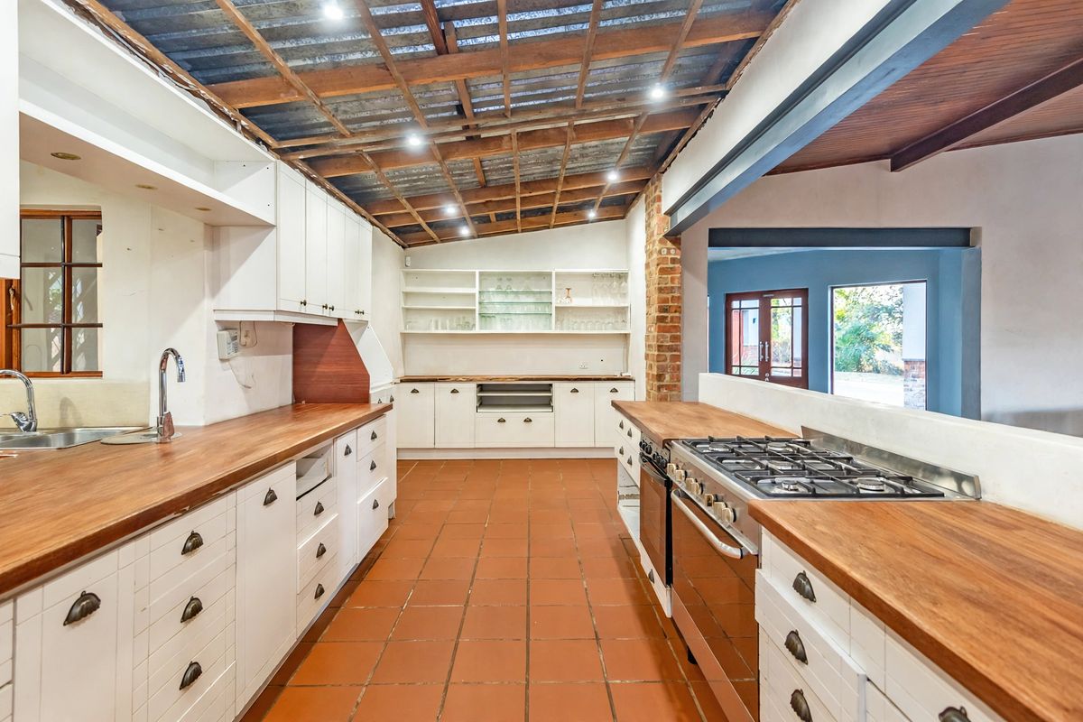 Spacious kitchen featuring wooden countertops, built-in cabinetry, gas hob, and exposed timber ceiling, offering a rustic aesthetic with potential for modern updates.