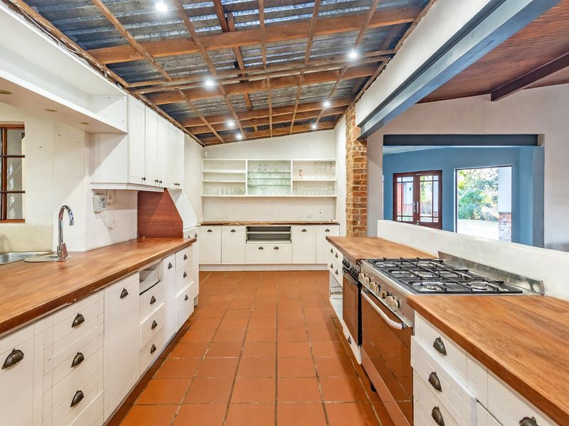 Spacious kitchen featuring wooden countertops, built-in cabinetry, gas hob, and exposed timber ceiling, offering a rustic aesthetic with potential for modern updates.