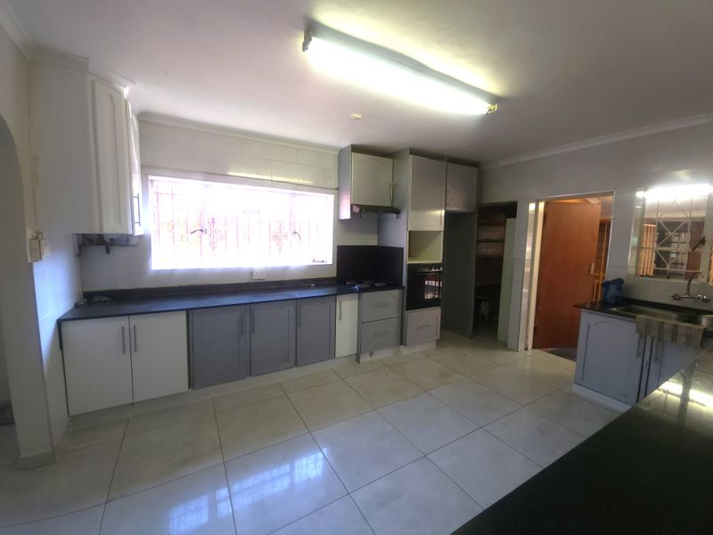 A functional kitchen featuring built-in cabinetry, laminate countertops, a built-in oven, hob, and a double sink with tiled flooring throughout.