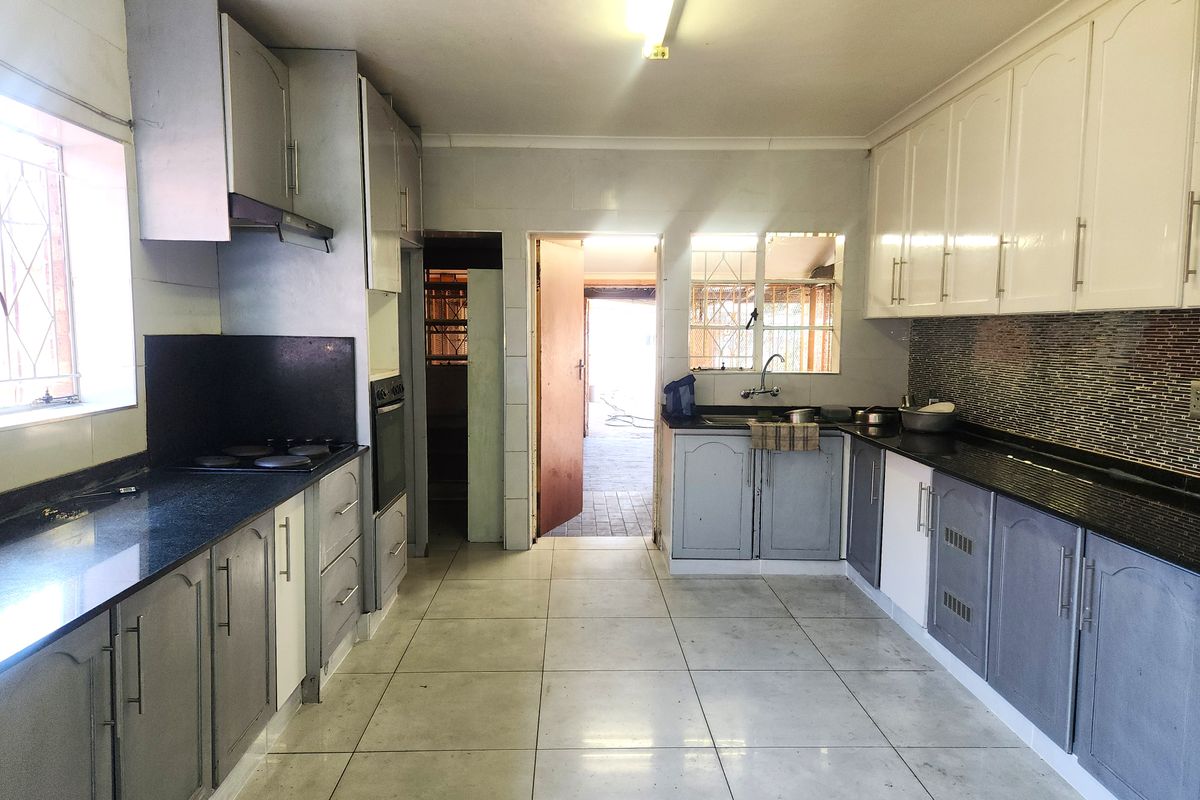 A functional kitchen featuring granite countertops, built-in cabinetry, an electric hob, and an oven, with direct access to an outdoor area.