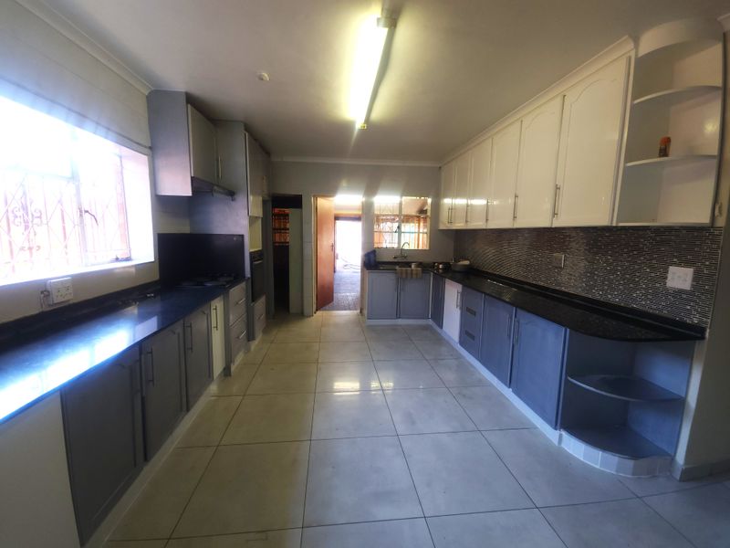 Spacious kitchen featuring extensive built-in cabinetry, granite countertops, mosaic tile backsplash, and ceramic floor tiles, offering a functional layout for meal preparation.