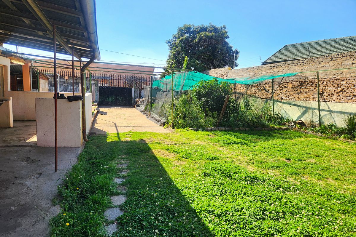 A rear garden area featuring a covered patio, lawn, and a brick boundary wall with shade netting structures.
