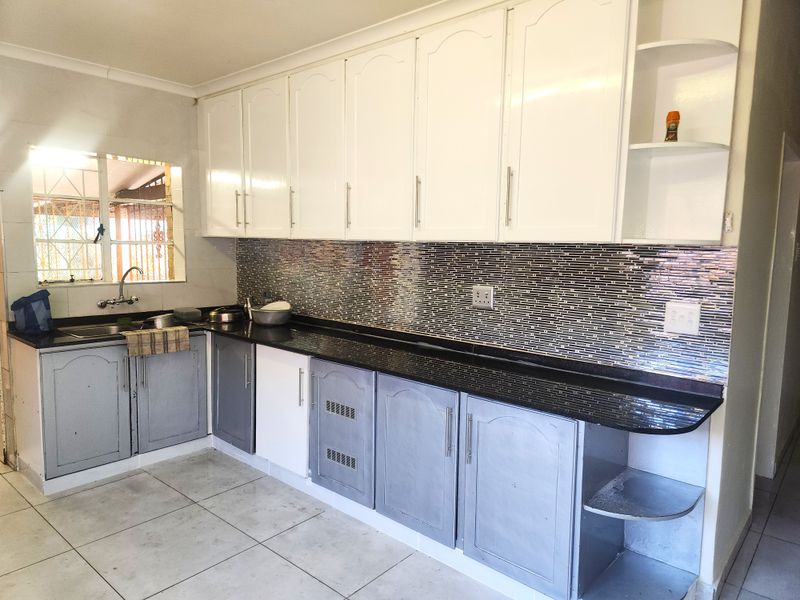 A functional kitchen featuring granite countertops, a mosaic tile backsplash, and ample built-in cabinetry with a mix of white and grey finishes.
