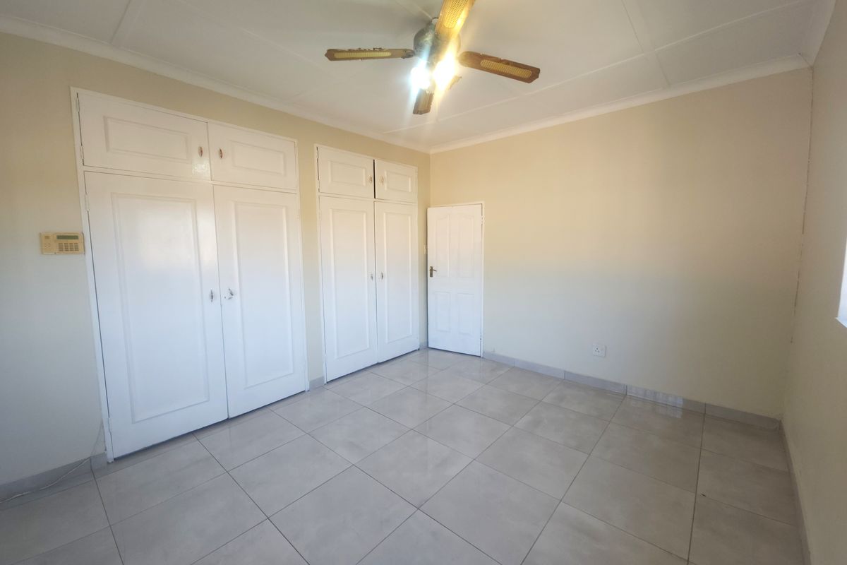 A spacious, empty bedroom featuring neutral tiled flooring, built-in storage cupboards, and a ceiling fan, offering a clean and versatile living space.
