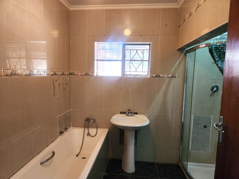 A functional bathroom featuring a pedestal basin, built-in bathtub, and a separate shower enclosure with tiled wall finishes.