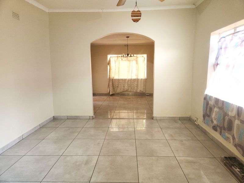 An open-plan living area featuring neutral tiled flooring and a central archway leading to an adjacent room.