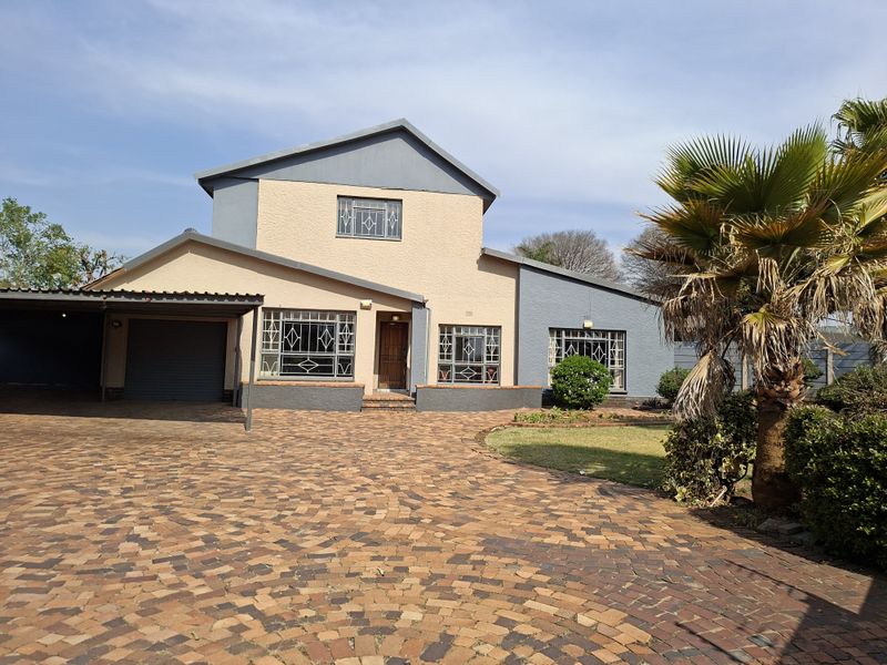 Front view of a multi-level residential house featuring a paved driveway, attached carport, and secure window treatments.