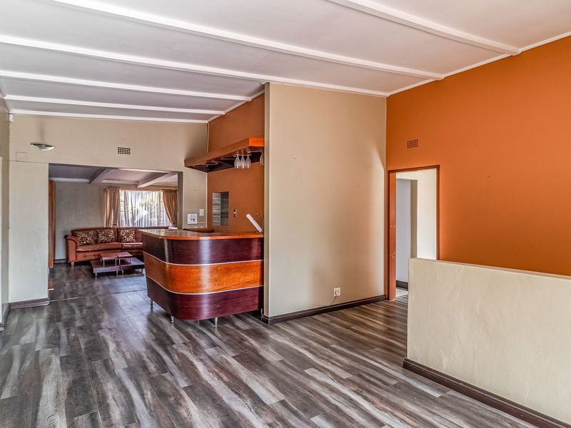 A living area featuring a built-in bar counter, wood-look laminate flooring, and an exposed beam ceiling, offering potential for a modern entertainment space.